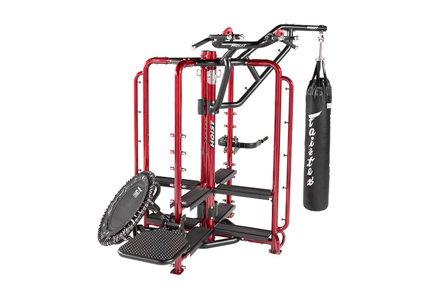 Red and black commercial workout cage with pull-up bar, heavy bag attachment, and dual-sided leg press machine on white backg