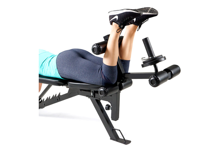 Person exercising on black Marcy utility weight bench with leg extension attachment, wearing navy leggings and black sneakers
