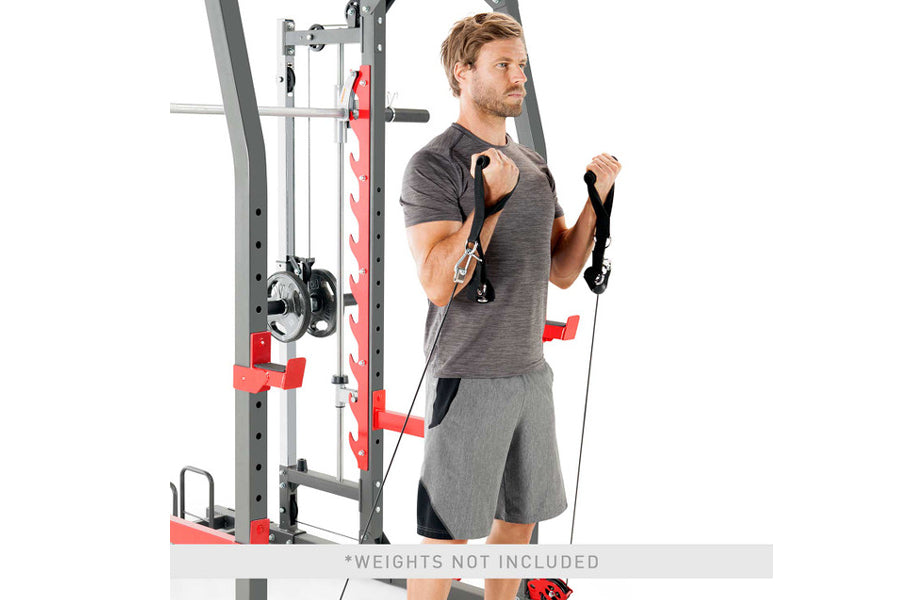 Man using gray and red Smith machine with cable attachments, wearing charcoal t-shirt and gray shorts