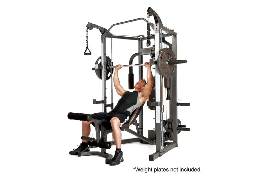 Man using gray and black Smith machine with weight bar, bench, and cable pulley attachment on white background