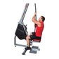 Man using gray and black vertical rope trainer machine with red seat, pulling rope overhead on white background