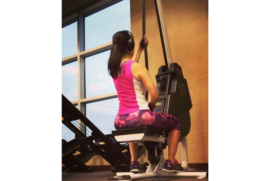 Woman wearing hot pink sleeveless top and burgundy patterned capris using Marpo VLT Compact Rope Trainer in gym setting with 