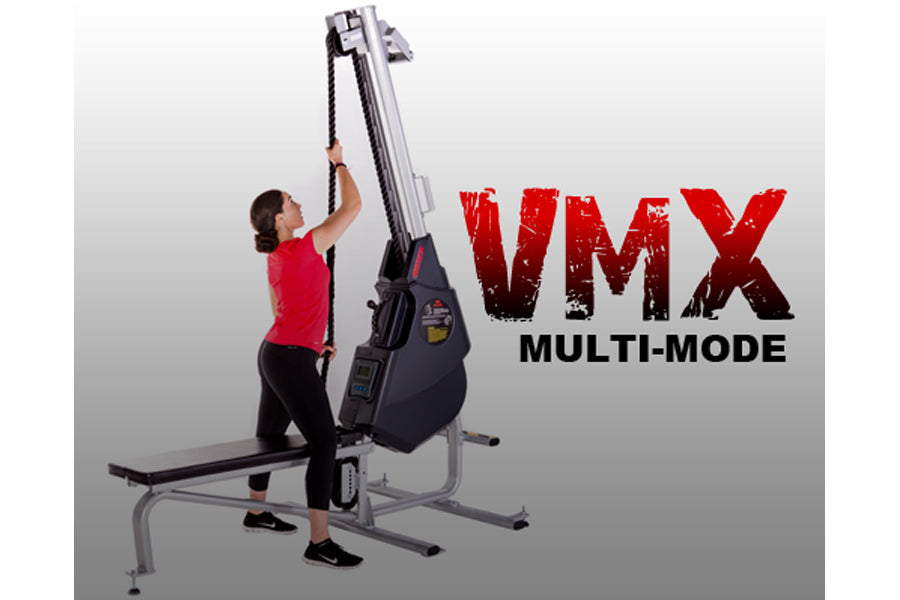 Woman in red shirt using black and gray VMX Multi-Mode rope trainer machine with extended arm mechanism on white background