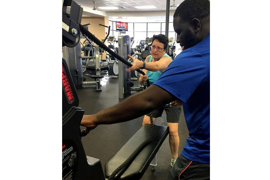 Personal trainer in blue shirt guiding man on Marpo VMX 360 rope trainer machine in gym setting