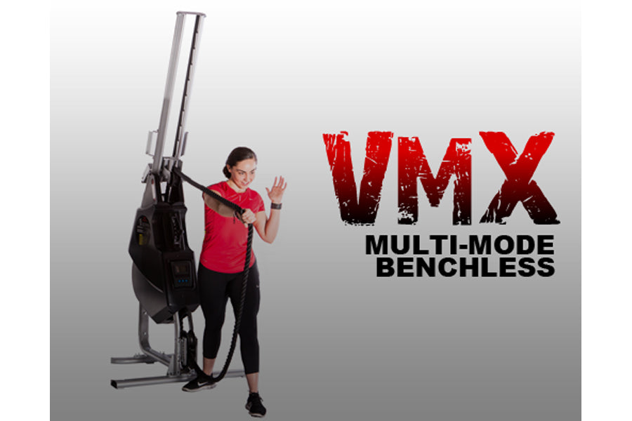 Woman in red shirt demonstrating black and silver VMX multi-mode benchless rope trainer machine on white background