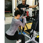 Woman using gray long-sleeve top exercising on Marpo VMX Rope Trainer in gym setting with instructor assisting
