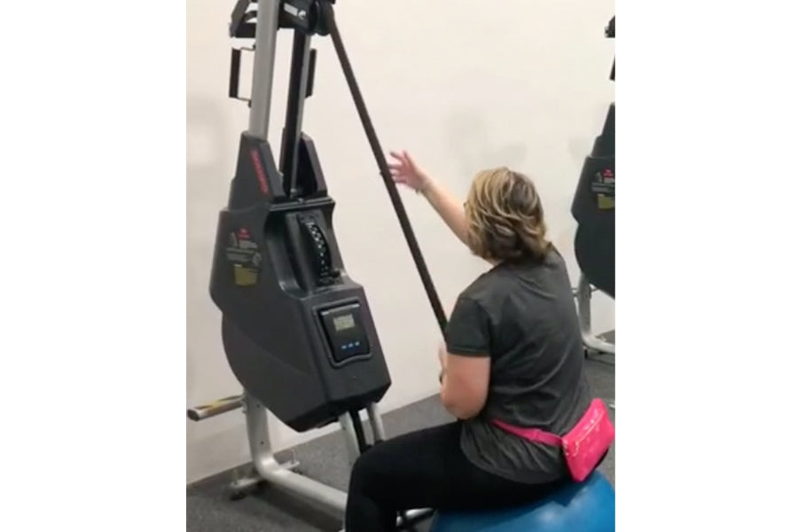 Woman using black and gray Marpo VMX rope trainer with digital display, worn with black shirt and neon pink waistband