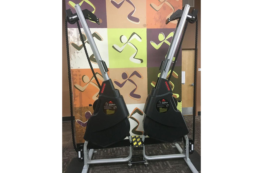 Pair of black Marpo VMX rope trainers with silver frames and yellow accents, displayed on stand against colorful abstract bac