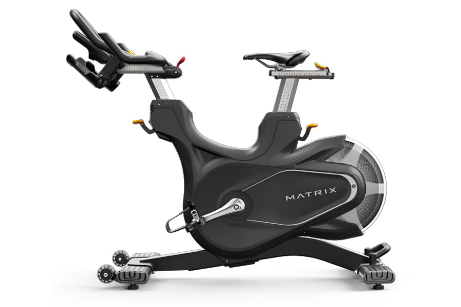 Matrix CXM indoor training cycle with black frame, padded seat, adjustable handlebars, and dual foot pedals on white backgrou