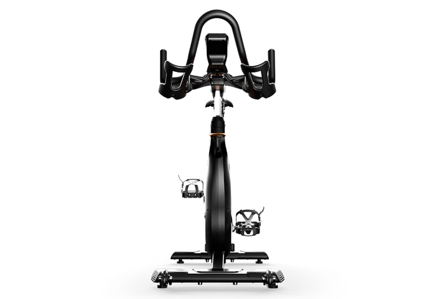 Black and white stationary indoor cycling bike with curved handlebars, digital display, and pedals shown from front view on w