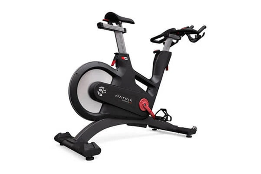 Matrix IC7 Indoor Club Group Cycle — angled rear view showing flywheel, adjustable saddle, multi-grip handlebars, red resistance knob, and arched stabilizing base