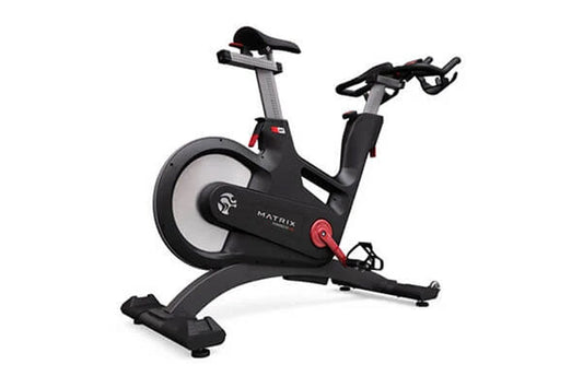 Matrix IC7 Indoor Club Group Cycle — angled rear view showing flywheel, adjustable saddle, multi-grip handlebars, red resistance knob, and arched stabilizing base