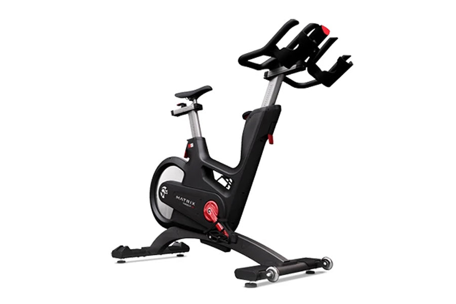 Matrix IC7 Indoor Club Group Cycle — side profile view showing multi-grip handlebars, adjustable saddle, red resistance knob, and transport wheels