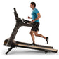 Man in blue t-shirt running on black Matrix T75 treadmill with gold accents against white background