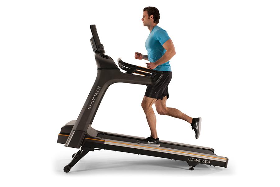 Man in blue t-shirt running on black Matrix T75 treadmill with gold accents against white background