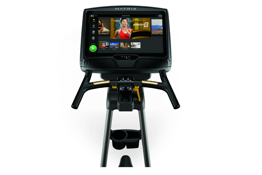 Matrix U50 upright exercise bike with black frame, yellow accents, and digital touchscreen display showing workout content, f