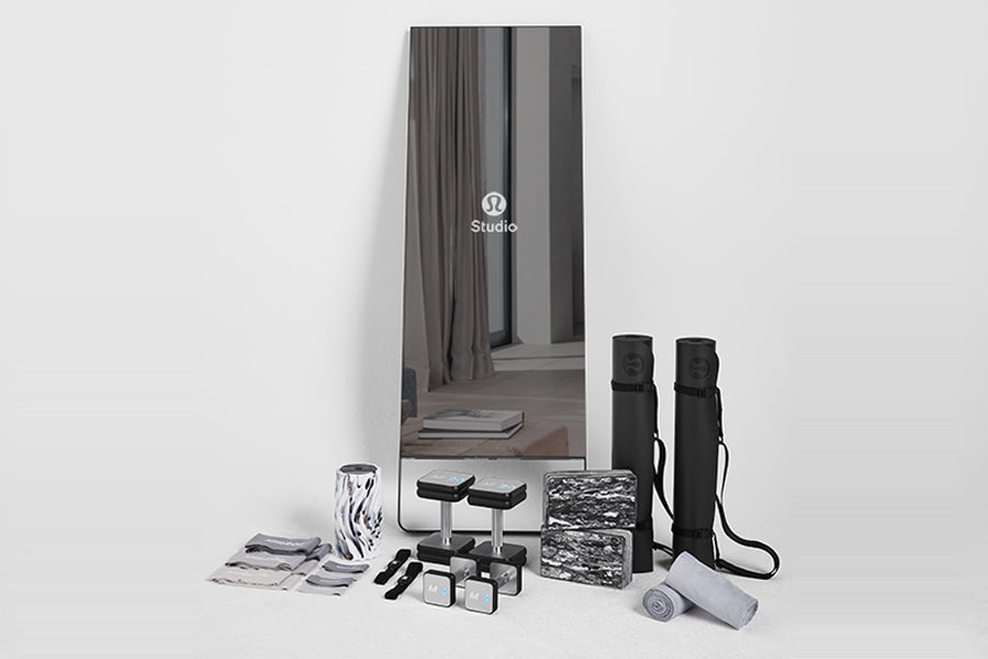 Lululemon Studio Mirror with black carrying cases, yoga mats, water bottle, towels, and accessories displayed on white backgr