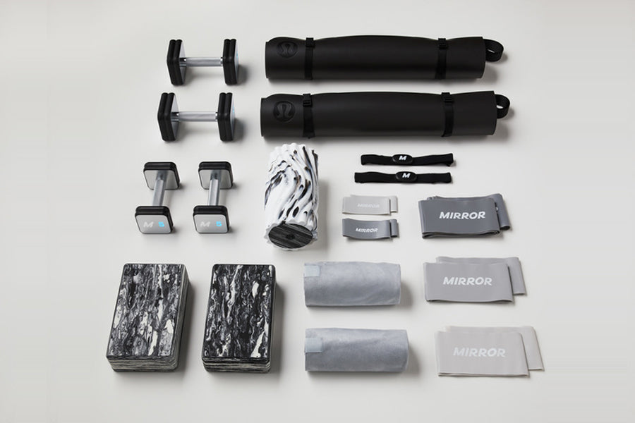 Lululemon Studio Mirror home fitness equipment set with dumbbells, resistance bands, roller, towels, and accessories arranged