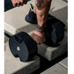 Person holding black adjustable dumbbell with neon green accents during outdoor workout
