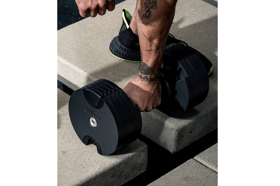 Person holding black adjustable dumbbell with neon green accents during outdoor workout