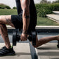Man performing dumbbell exercise with black adjustable weights and black sneakers in outdoor setting