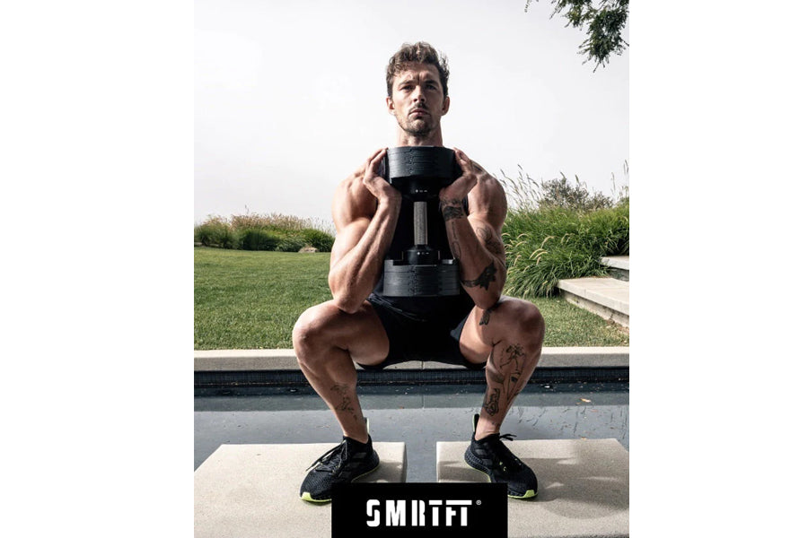 Male athlete performing squat exercise with black adjustable dumbbell, outdoor setting with pool and grass background