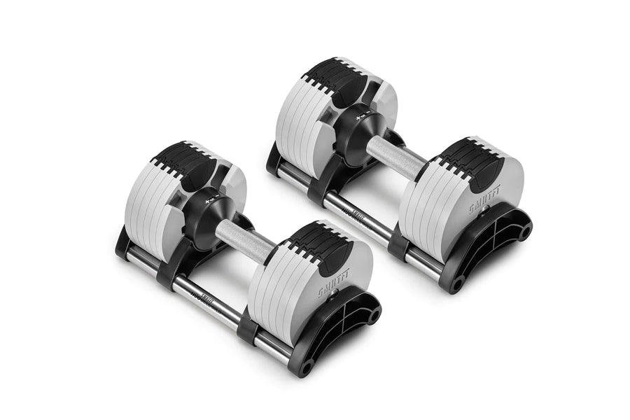 Pair of NÜOBELL adjustable dumbbells with white weight plates, black caps, and metal handles on black bases, shown on white b