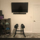 Black adjustable dumbbell stand with double legs holding two dumbbells in home gym setting