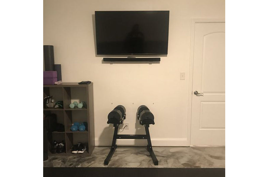 Black adjustable dumbbell stand with double legs holding two dumbbells in home gym setting