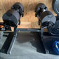 Pair of black and gray adjustable dumbbells mounted on black NÜOBELL stand with double legs, on wooden floor