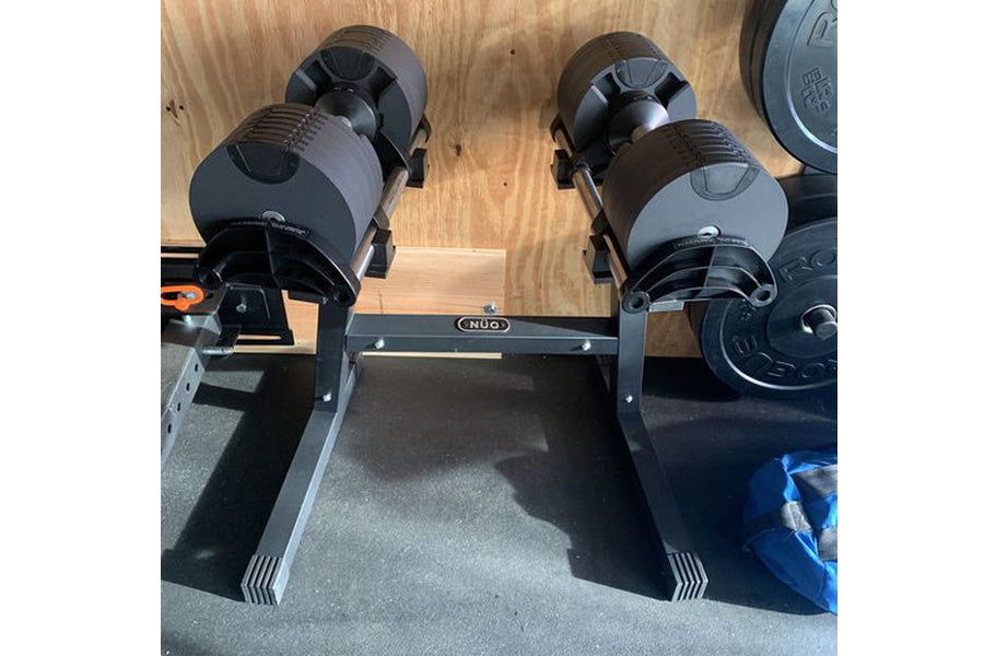 Pair of black and gray adjustable dumbbells mounted on black NÜOBELL stand with double legs, on wooden floor