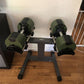 Pair of sage green adjustable dumbbells mounted on black single-legged stand with NUO branding, on wooden floor