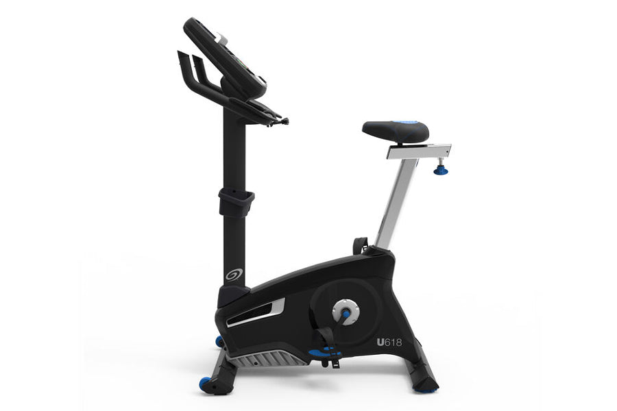 Black and silver upright exercise bike with padded seat, handlebar arms, and digital display console on white background
