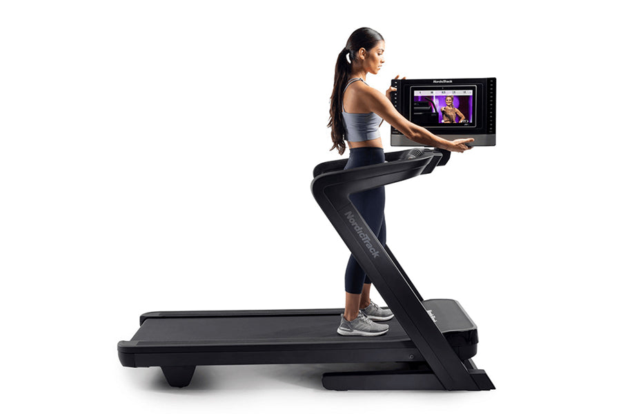 Woman in athletic wear running on black NordicTrack treadmill with touchscreen display showing workout content