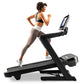 Woman running on black NordicTrack treadmill with digital display, wearing black sports bra and taupe leggings