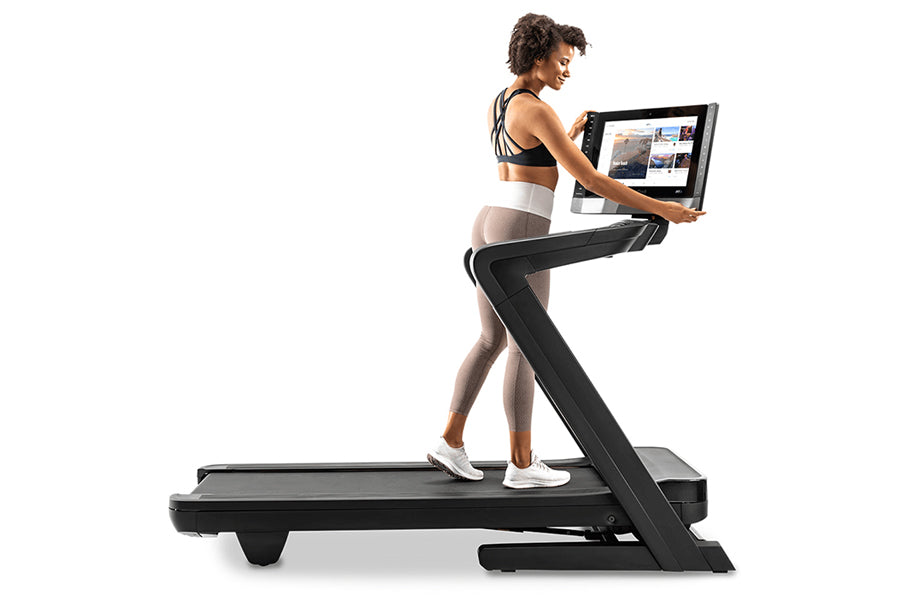 Woman in black and white athletic wear running on black NordicTrack treadmill with tablet display mounted on console