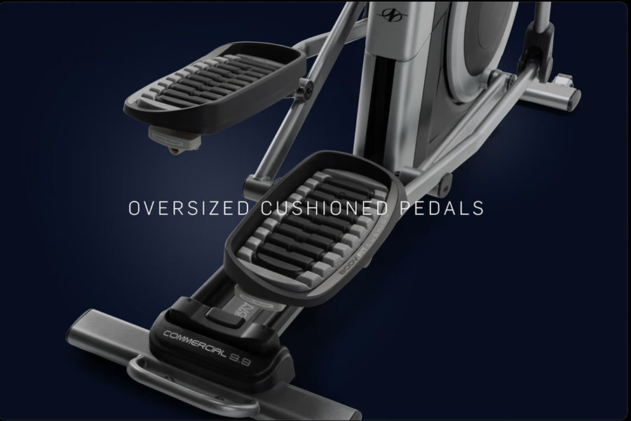 Silver and black elliptical machine with oversized cushioned pedals on dark blue background