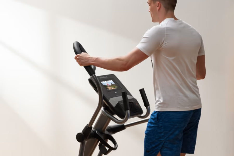 Man wearing white t-shirt using black NordicTrack elliptical with digital display console