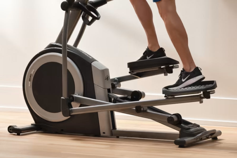 Person wearing black sneakers on NordicTrack commercial elliptical with black and gray frame on wooden floor