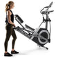 Woman using black and silver NordicTrack elliptical machine with dual handles and large foot pedals on white background