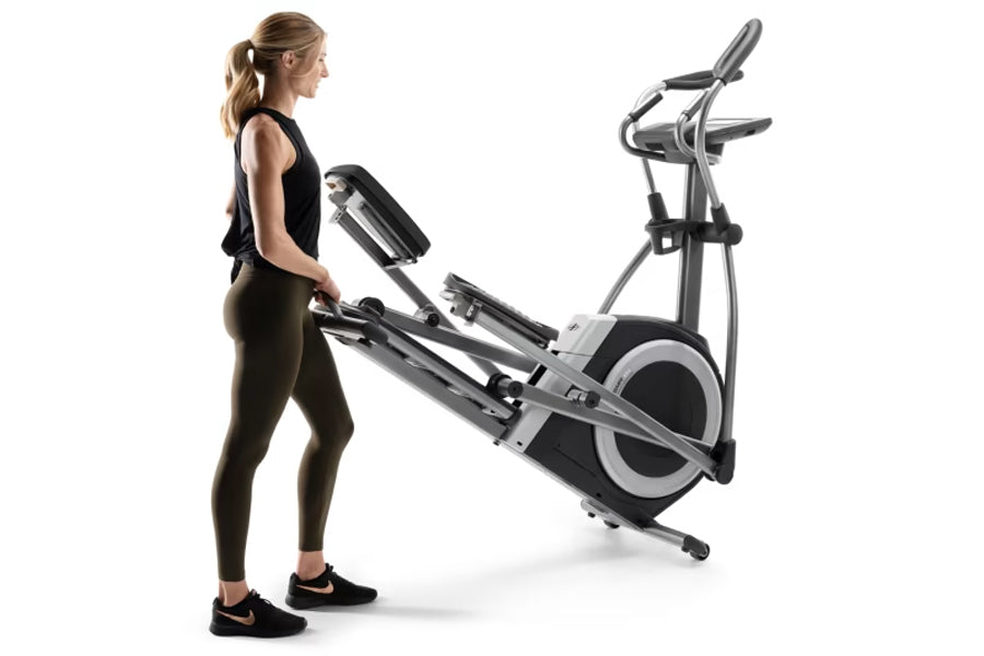 Woman using black and silver NordicTrack elliptical machine with dual handles and large foot pedals on white background