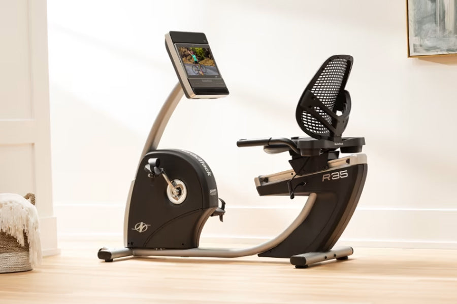 NordicTrack Commercial R35 black and tan recumbent exercise bike with tablet holder, shown on wooden floor in home setting