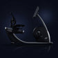 Black and silver recumbent exercise bike with curved frame, digital console, and pedal platform on dark background