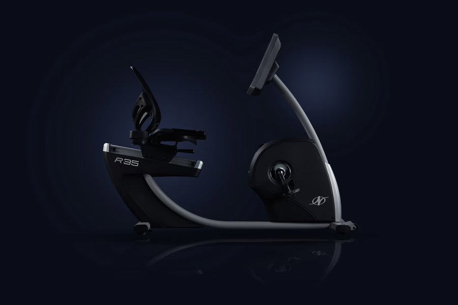 Black and silver recumbent exercise bike with curved frame, digital console, and pedal platform on dark background
