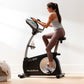 Woman in gray sports top and brown leggings using black and silver NordicTrack VU 29 upright exercise bike with digital displ