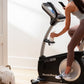 Woman in gray tank top and brown leggings using black and silver NordicTrack VU 29 upright exercise bike with digital display