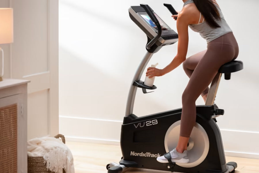 Woman in gray tank top and brown leggings using black and silver NordicTrack VU 29 upright exercise bike with digital display