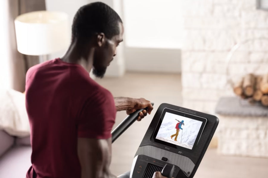 Man in burgundy t-shirt using NordicTrack FS10i elliptical with touchscreen display in home setting