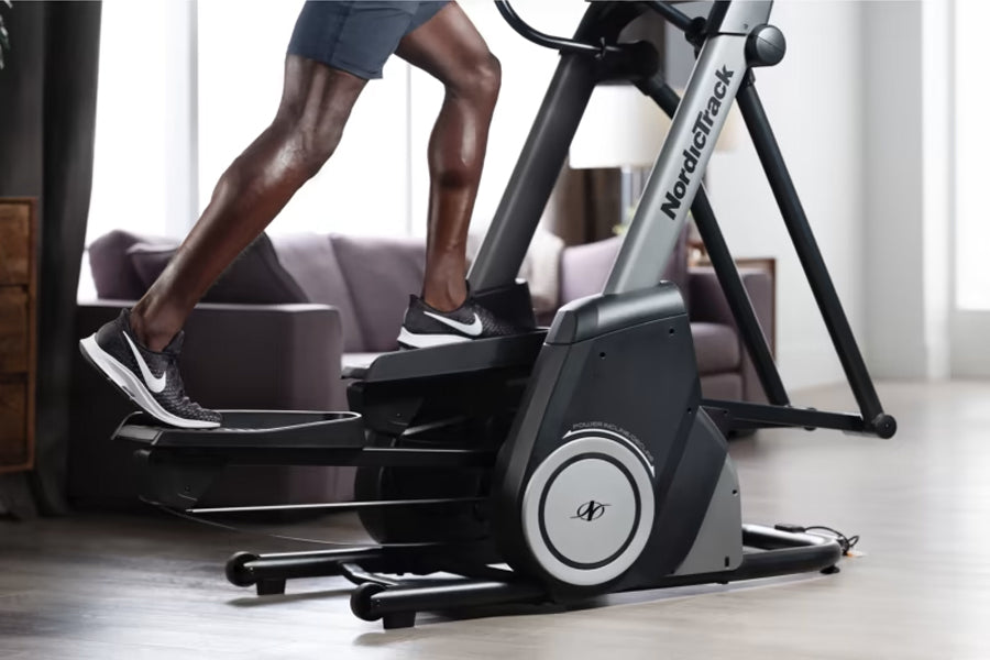 Person using black and silver NordicTrack FS10i elliptical machine in home gym setting