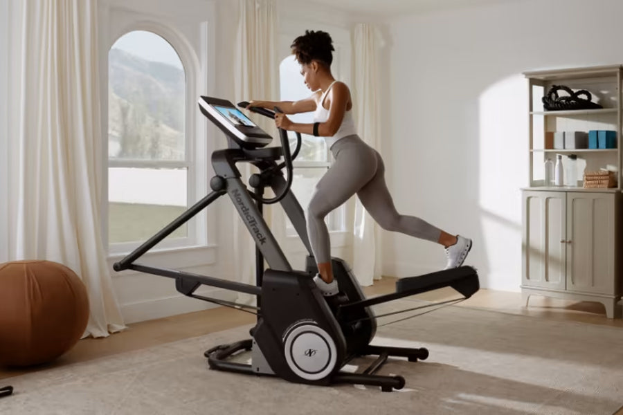 Woman using black NordicTrack FS14i elliptical machine with digital display in bright home gym setting